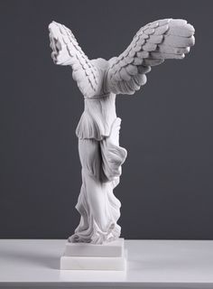 an angel statue on a white pedestal with wings spread around its body and head, in front of a gray background