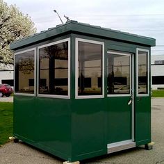 a small green building sitting on the side of a road next to a parking lot