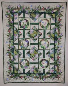 a green and white quilted wall hanging with flowers on the border, two faces are in the center