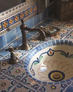 a bathroom sink with blue and white tiles on the counter top, along with two faucets