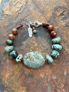 "Genuine African turquoise beads are hand knotted on a brown silk thread with a snakeskin jasper centerpiece! Antique brown hued glass beads round out the piece. Handmade leather thread guards protect the thread at the pressure points and add to the rustic look to the bracelet. A cool sunburst \"cog\" acts as a decorative end piece. You can clasp the large sterling silver clasp on the cog or the other rings, so the bracelet is between 7 and 7 1/2 inches. The feather charm, clasp, and jump rings Snakeskin Jasper, African Turquoise, Leather Thread, Pretty Jewelry, Feather Charms, Brown Silk, Pressure Points, Silk Thread, Etsy Jewelry