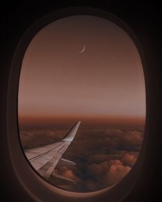 an airplane window looking out at the sky and clouds with a half moon in the distance