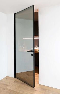 an open glass door in the corner of a room with wood flooring and white walls