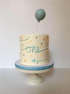 a one year old birthday cake on a pedestal with a balloon flying over the top