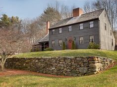 a large house with a stone wall in front of it and trees around the yard