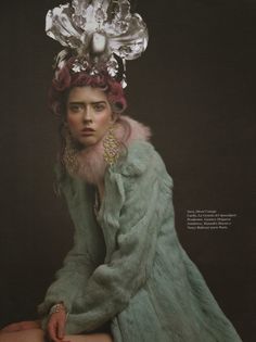 a woman in a fur coat and headdress sitting on a stool with her legs crossed