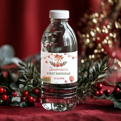 a bottle of water sitting on top of a table next to holly branches and red berries