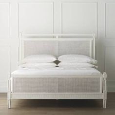 a white bed with two pillows on top of it and a wooden floor next to it