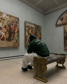 a man sitting on a bench in front of paintings