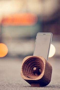 a wooden device holder with a cell phone in it sitting on the ground next to a street