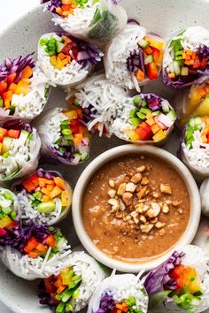 a white plate topped with rolls covered in veggies and peanut butter dipping sauce