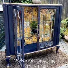 an old china cabinet painted in blue and gold with potted plants on the top