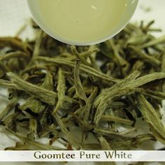 a spoon full of white tea sitting on top of a pile of green leaves