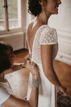 a woman helping another woman put on her wedding dress