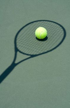 a tennis ball and racket casting a shadow on the court