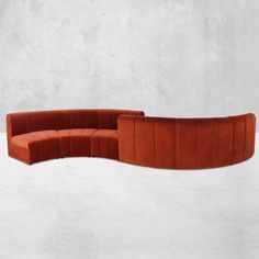 an orange curved couch sitting on top of a white floor next to a cement wall