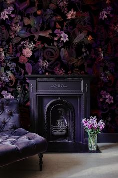 a purple chair sitting next to a fireplace in front of a wall with flowers on it