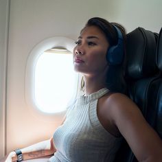 a woman sitting in an airplane with headphones on her ears and looking out the window