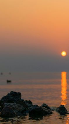 the sun is setting over the ocean with rocks in the foreground