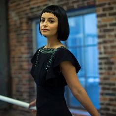 a woman standing in front of a window wearing a black dress and pearls on her neck