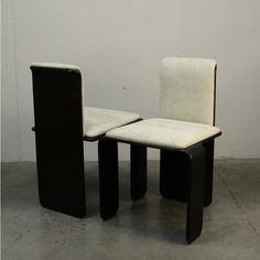 two black and white chairs sitting next to each other on cement floored area with wall in background