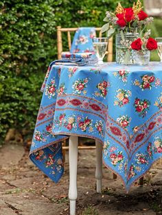 a blue table cloth with red flowers on it and a vase full of roses in the background