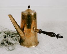 an old brass teapot with a wooden handle next to it on a white furnishing