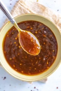 a spoon full of chili sauce on top of a bowl with a napkin underneath it