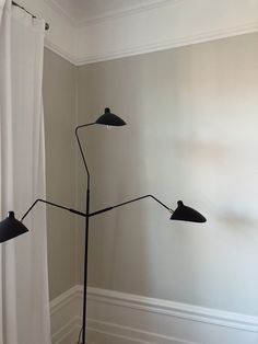 a floor lamp in the corner of a room next to a window with white curtains