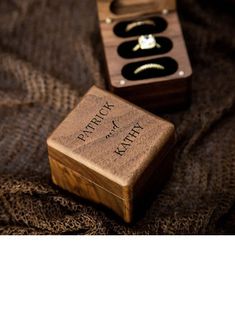 an open wooden box sitting on top of a bed next to a ring box with two wedding rings in it