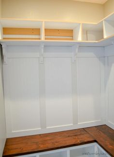 an empty room with white walls and wooden bench in the center, along with shelving