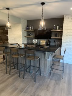 a kitchen with an island and bar stools next to it, in front of a brick wall