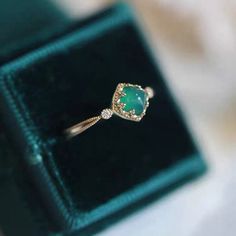 an engagement ring with a green stone and diamond accents in a velvet box on top of a table