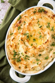 a casserole dish with cheese and parsley in it on a green cloth