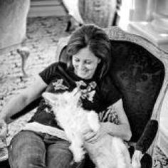 black and white photograph of woman sitting in chair with two dogs, one is holding the other's head