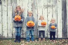 three children holding pumpkins in front of a fence