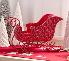 a red sleigh sitting on top of a wooden table next to christmas trees