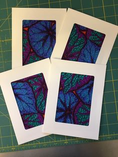 four cards with blue and purple leaves are on a cutting board next to a knife