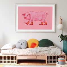 a pink pig print hangs above a bed in a child's room with toys