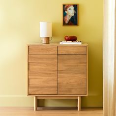 a wooden cabinet with a painting on the wall above it and a lamp next to it