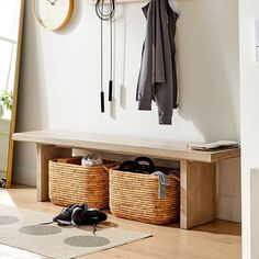 a bench with two baskets underneath it next to a clock and coat rack on the wall