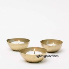 three metal bowls with candles in them on a white surface