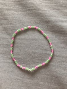 a pink and green beaded bracelet on top of a gray cloth covered bed sheet