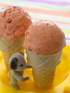 two ice cream cones on a yellow plate with an elephant figurine next to them