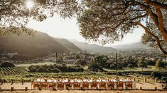 an outdoor dining table set up in the middle of a field with mountains behind it