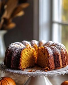 a bundt cake with one slice cut out on a plate next to two pumpkins