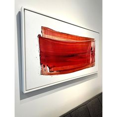 an abstract painting hangs on the wall next to a white framed art piece with red paint