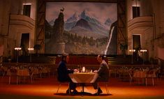 two people sitting at a table in front of a large screen with mountains on it