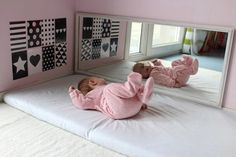 a baby laying on top of a bed in front of a mirror