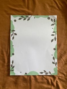 an empty piece of paper with leaves on it sitting on a brown sheet of fabric